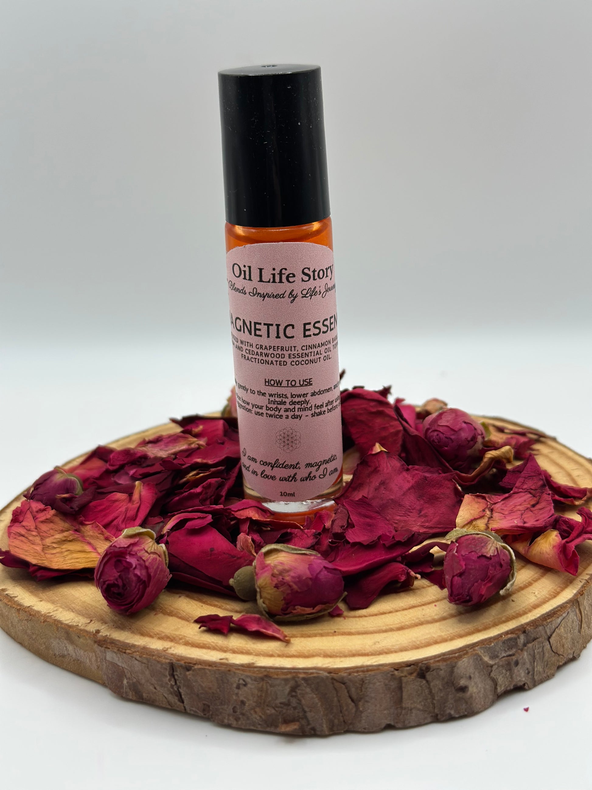 Magnetic Essence essential oil blend on a wooden plate, surrounded by dried red rosebuds